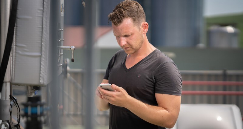 Landwirt auf sein Handy schauend steht vor der Biogasanalage